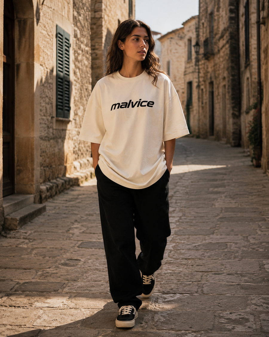 Woman wearing an ivory MALVICE T-shirt in a sunlit stone street