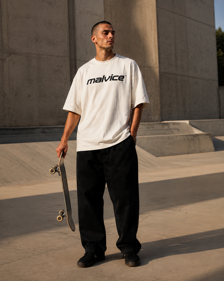 Man wearing a white MALVICE T-shirt at a concrete skate plaza