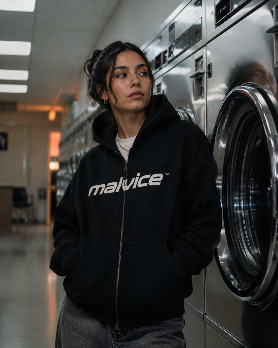 Woman wearing a black MALVICE hoodie in a modern laundromat