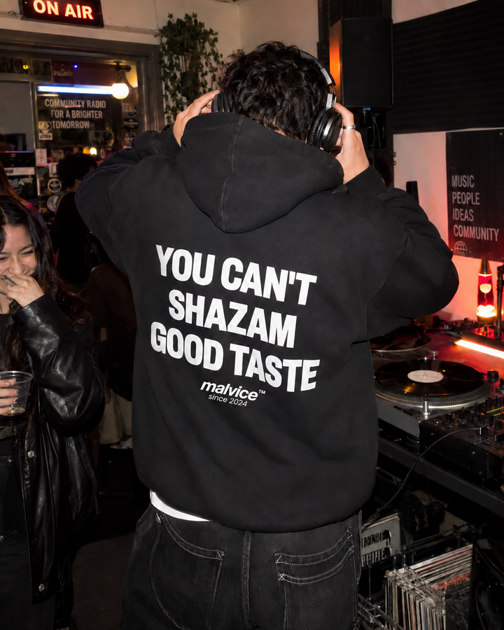 Man wearing a black MALVICE You Can't Shazam Good Taste hoodie at a community radio party