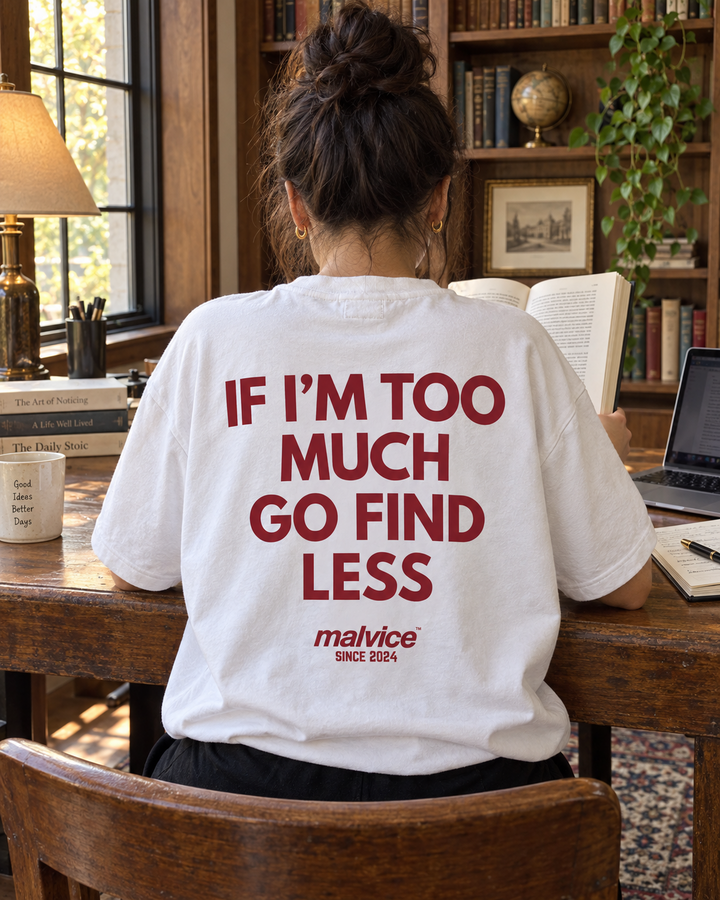 Woman wearing a white MALVICE If I'm Too Much Go Find Less oversized T-shirt in a library