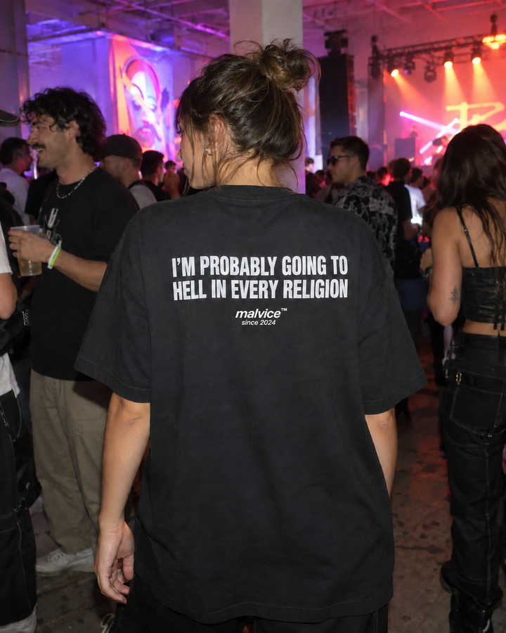 Woman wearing a black MALVICE I'm Probably Going to Hell in Every Religion oversized T-shirt at a warehouse music party